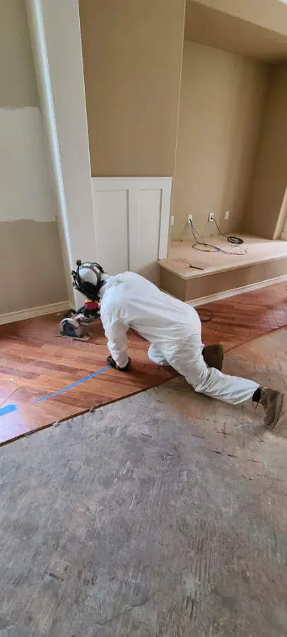 Technician in Tyvek suit removing hardwood flooring with a power tool during water damage restoration