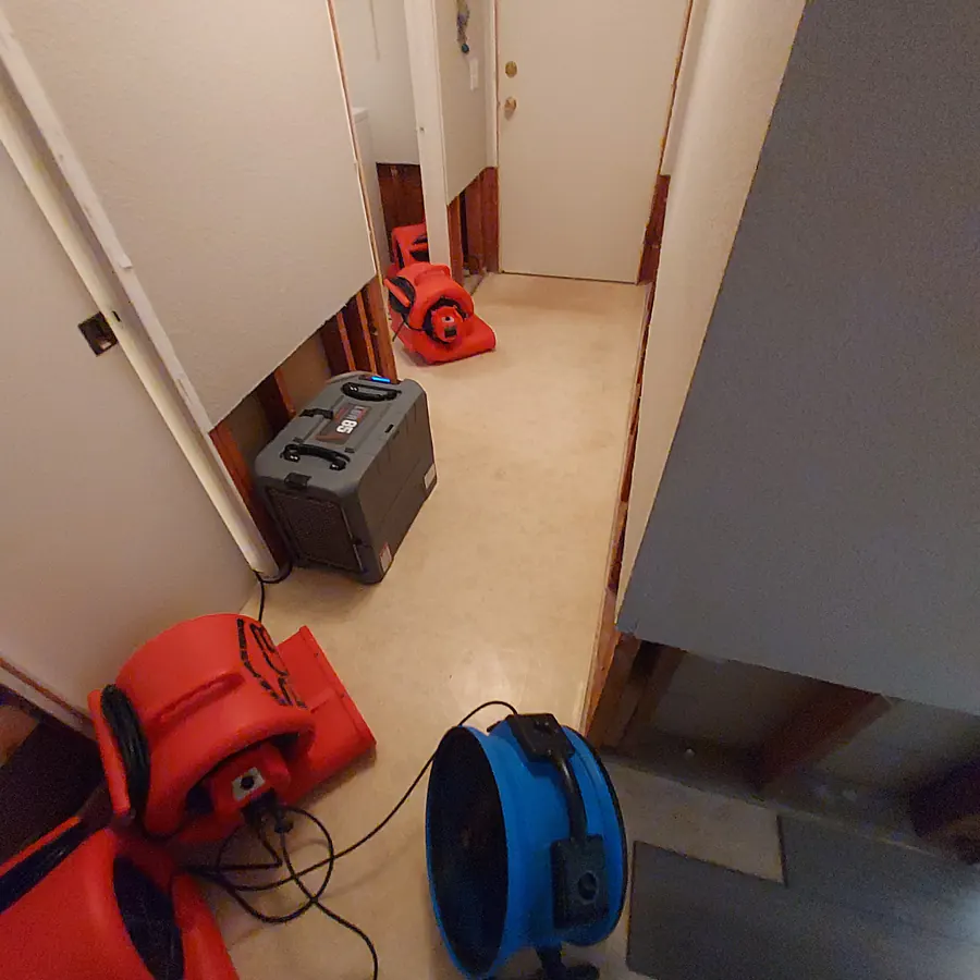 Residential hallway during active dryout with RCR-branded air movers and dehumidifier along flood-cut walls