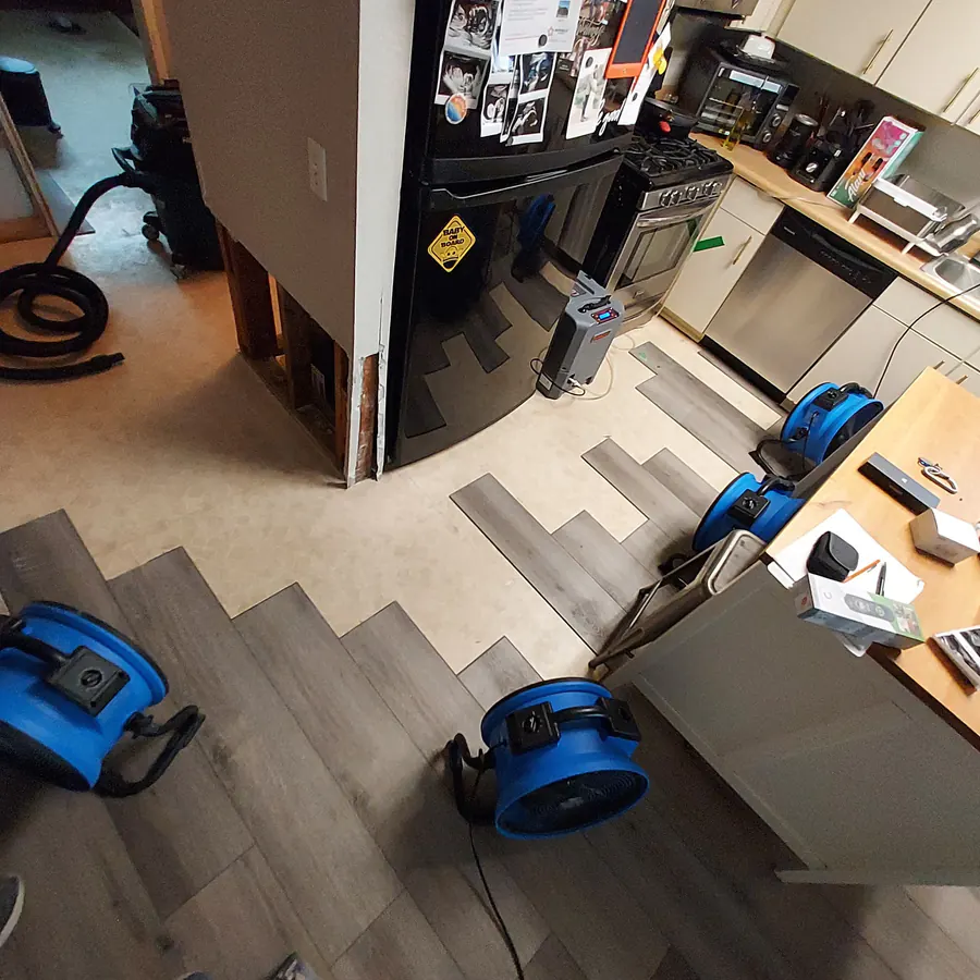 Kitchen water damage restoration with air movers and floor removal in progress