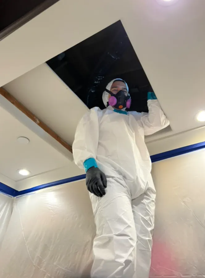 Technician in Tyvek suit and respirator inside containment area during water damage restoration